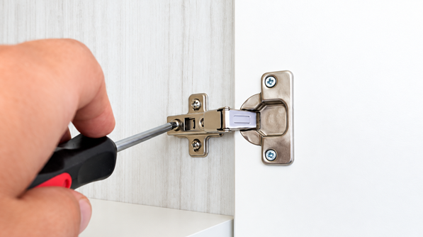 Person Installing Cabinet Hinge with Screwdriver Inside Kitchen